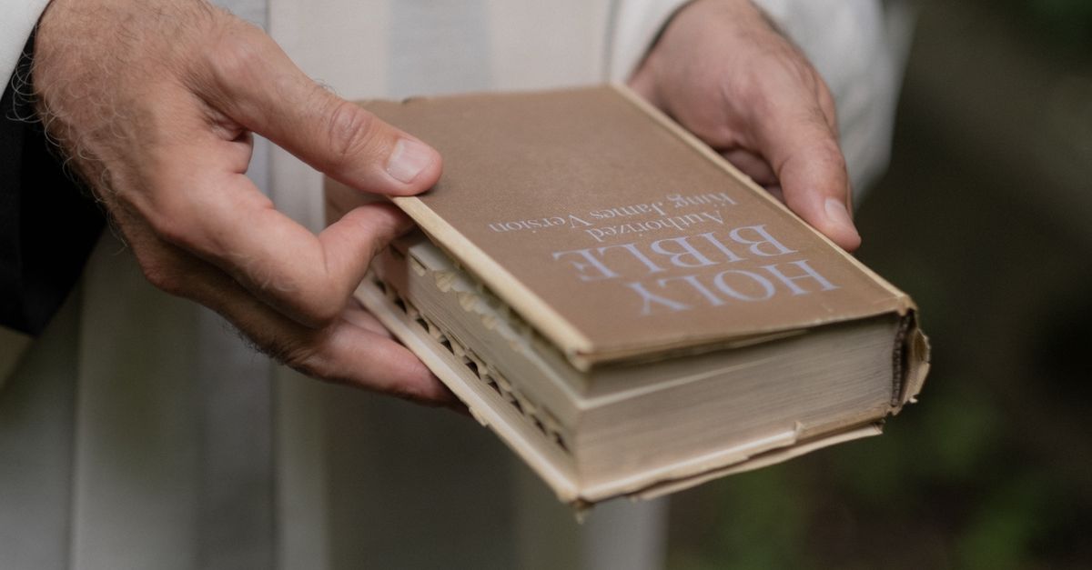 An elderly person gently holds a well-worn Holy Bible in their hands.